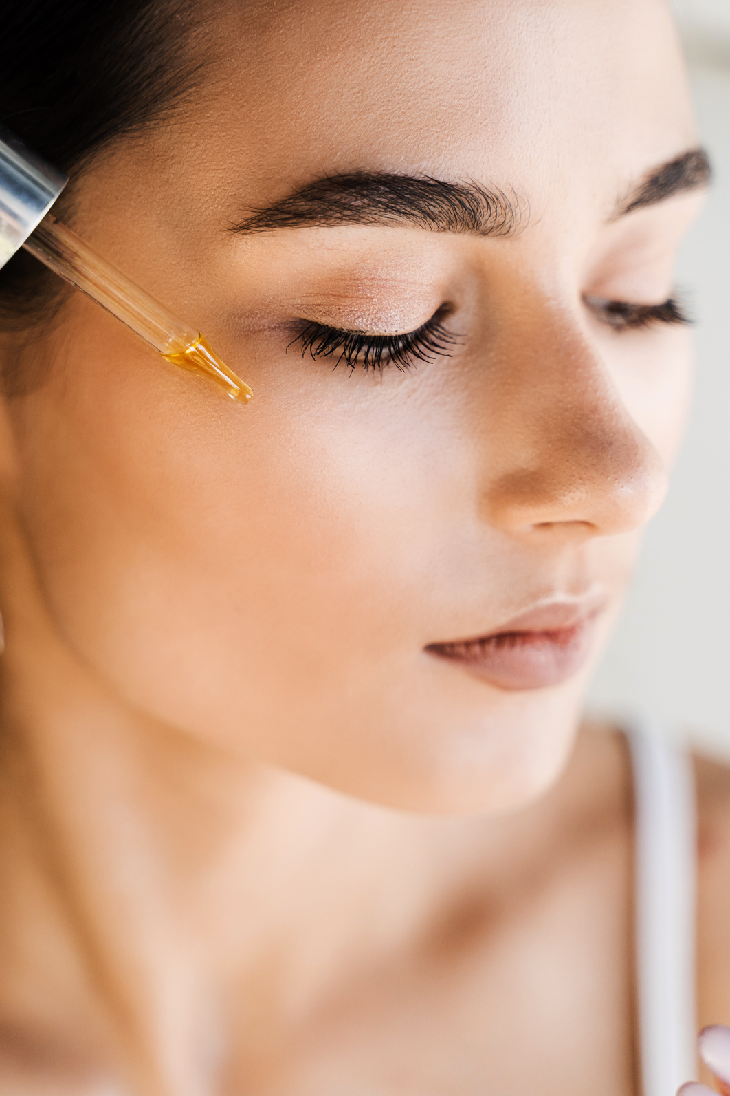 Girl applying hyaluronic serum with pipette on face. Young woman with acid dropper is applying drops of acid on her skin.