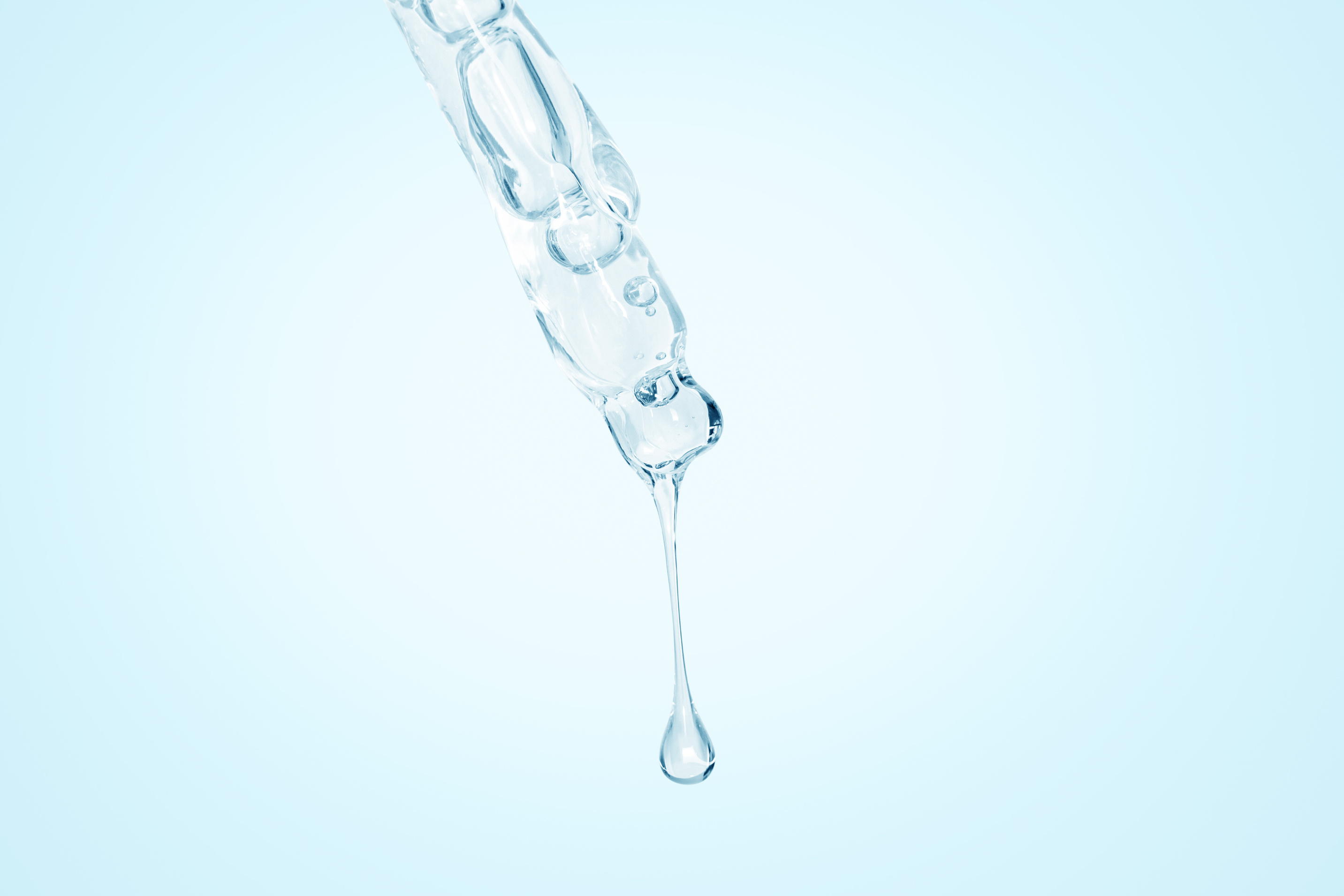 Cosmetic pipette with dripping liquid and drops on the south, blue background, serum, serum, gel, vitamin, water, oil.